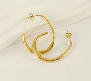 Detailed view of chunky U-shape 18K gold-plated stainless steel earrings on a beige surface