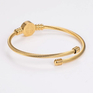 Detail of gold twisted cable open bangle featuring a round embossed charm pendant