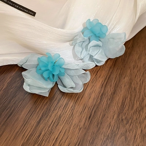 Dettaglio di orecchini a fiore in tulle blu con petali stratificati e centro opaco