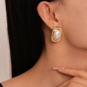 Close-up of model wearing gold square earring with large white oval pearl inlay