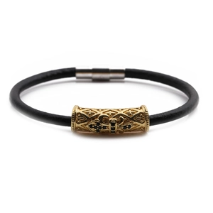 Close-up of leather bracelet featuring a gold cylinder charm with cross engraving