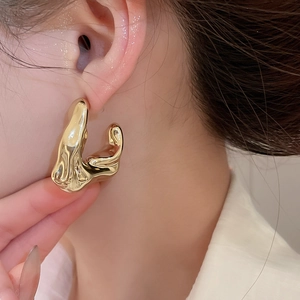 Close-up of golden irregular liquid-metal style earring on model with glossy finish