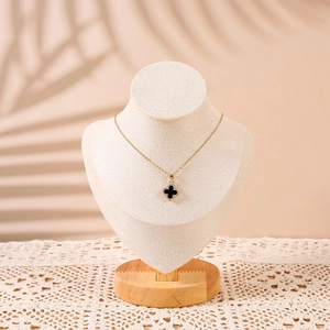 Detail of a gold necklace with a black clover pendant on a solid wood neck bust display