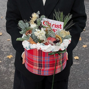 Christmas-themed gift bucket with pine cones and cinnamon held against a dark coat