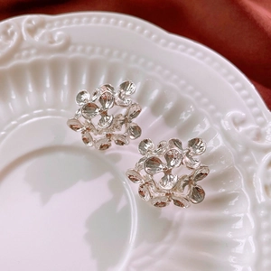 Close-up of silver floral hoop earrings with a hammered texture on a vintage white plate