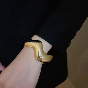 Dettaglio di un bracciale rigido dorato a onde dal design minimalista sul polso del modello