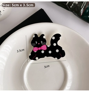 Detailed view of polka dot cat hair clip with pink bow in a white ceramic dish