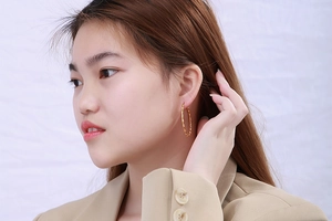 Close-up of golden bamboo texture hoop earrings worn by a model in a beige blazer