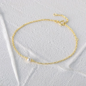 Macro view of dainty gold-plated chain bracelet with a single round white pearl