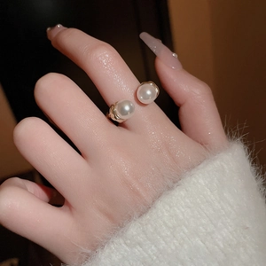 Close-up of dual pearl open ring in gold finish worn with a cozy white sweater