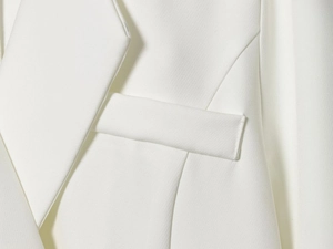 Detail of white woven blazer featuring a tailored collar and a classic welt pocket