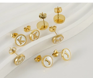 Macro view of gold stainless steel initial earrings with white shell inlay details
