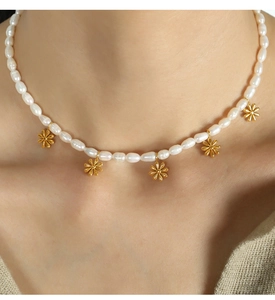 Detail of freshwater pearl necklace with golden daisy pendants on a woman's collarbone