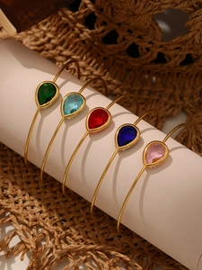 Close-up of five colorful pear-cut glass stones on gold stainless steel open bangles