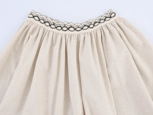 Détail de la taille d'une jupe en lin beige avec des bordures tressées à vagues noires