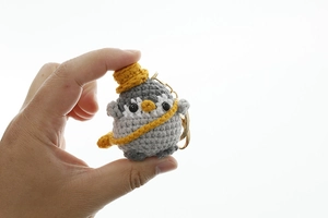 Close-up of a handmade crochet penguin keychain with a yellow hat and metal ring