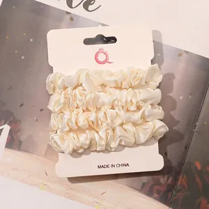 Close-up of four-piece beige satin scrunchie set on a white display card in soft lighting