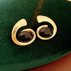 Detail of gold geometric spiral earrings with black oval stones on green velvet