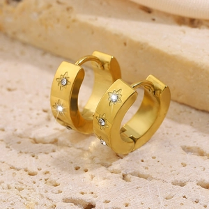 Polished gold plated starburst earrings with sparkling zircon on natural stone background
