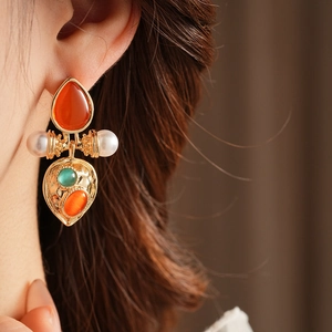 Detail of vintage palace style earring with green gemstone and cat-eye stone on model