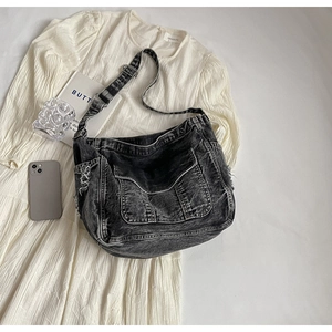 Détail d'un sac bandoulière en denim noir vieilli avec des franges et une poche à rabat