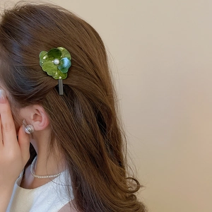 Gros plan d'une pince à cheveux fleur verte avec perle sur cheveux ondulés