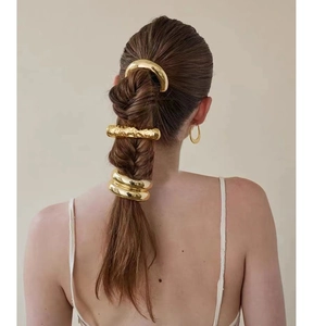Detail showing various textures of golden metal hair ring accessories on a low ponytail