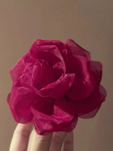 Dettaglio di un fermaglio per capelli a rosa in tessuto rosso scuro tenuto a mano