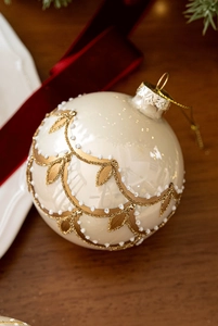 Detail of 8cm cream Christmas glass ball with gold glitter vine patterns on festive background