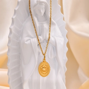 Detailed shot of 18K gold plated sun pendant necklace draped on a white statue sculpture