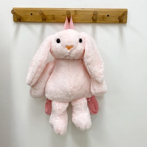 Pink plush rabbit backpack with long ears and adjustable straps on a wooden wall hook
