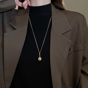 Close-up of a minimalist gold ball pendant necklace worn over a dark brown blazer