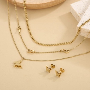 Three-layer gold butterfly pendant necklace and matching earrings set on a rustic stone base