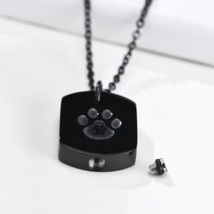 Close-up of black stainless steel cremation pendant with paw print and unscrewed cap