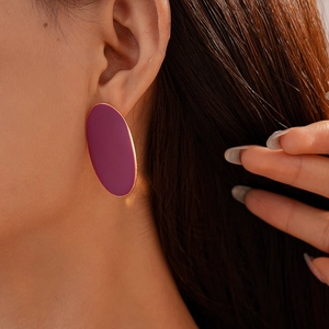 Macro view of purple oval geometric stud earrings with gold trim on a model ear