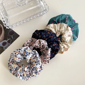 Detailed view of five floral print scrunchies in diverse colors and soft fabric textures