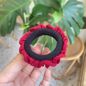 Detailed close-up of a red pleated fabric scrunchie with elastic inner band being held