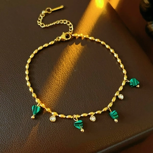Détail d'un bracelet doré vintage avec pierres de cœur vertes sur cuir marron