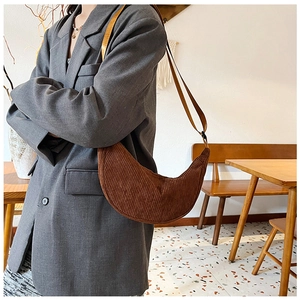 Brown corduroy crescent bag shown on model with adjustable strap in bright cafe setting