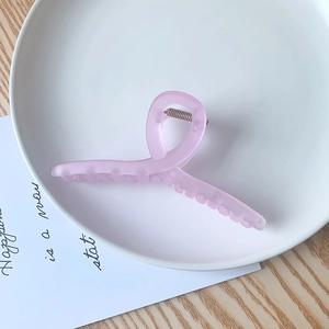 Détail d'une grande pince à cheveux rose mat posée sur un plateau décoratif blanc