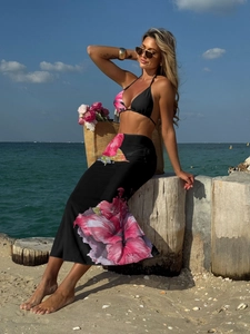 Detail view of the floral print mesh skirt and bikini set on a tropical beach background