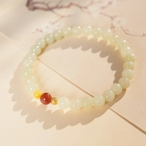 Detail of white Hetian jade bracelet with gold, red, and yellow beads on floral paper
