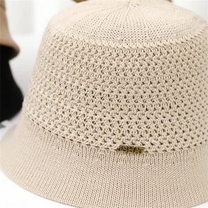 Close-up of beige knitted bucket hat with hollow mesh texture and metal letter logo