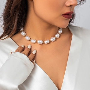 Detail of white baroque pearl necklace with gold metal clasp on a white silk top