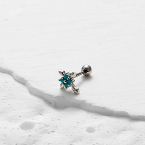 Close-up of a silver cross stud earring featuring turquoise stone on white stone surface