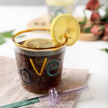 Detail of a glass dessert cup with gold rim and colorful 3D Love text inside a cozy setting