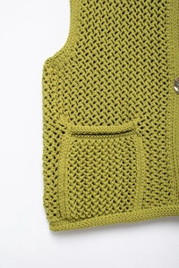 Detailed macro view of green knit vest showing coarse texture, pocket and gold button