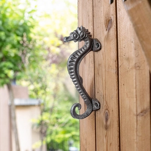 Vintage seahorse cast iron door handle mounted on a rustic wooden cabinet door