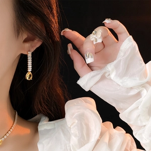 Detail of elegant gold earrings with yellow teardrop zircon on a model with bow nail art