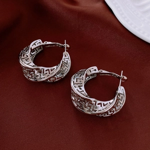 Macro shot of silver hollow Greek Key pattern hoop earrings on dark red fabric